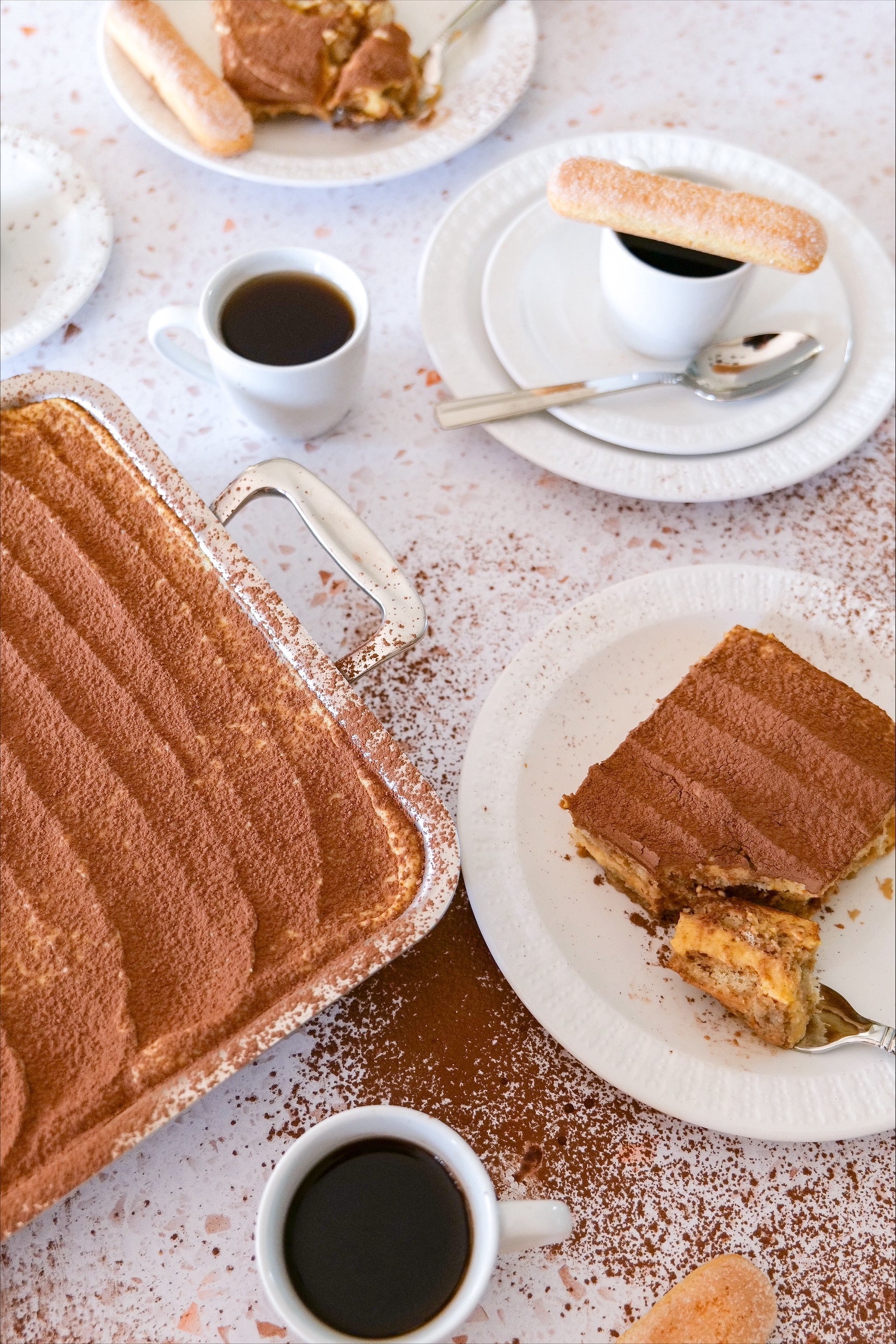 Pumpkin tiramisu in a serving pan and on a plate, cocoa-dusted slices with espresso cups and ladyfingers