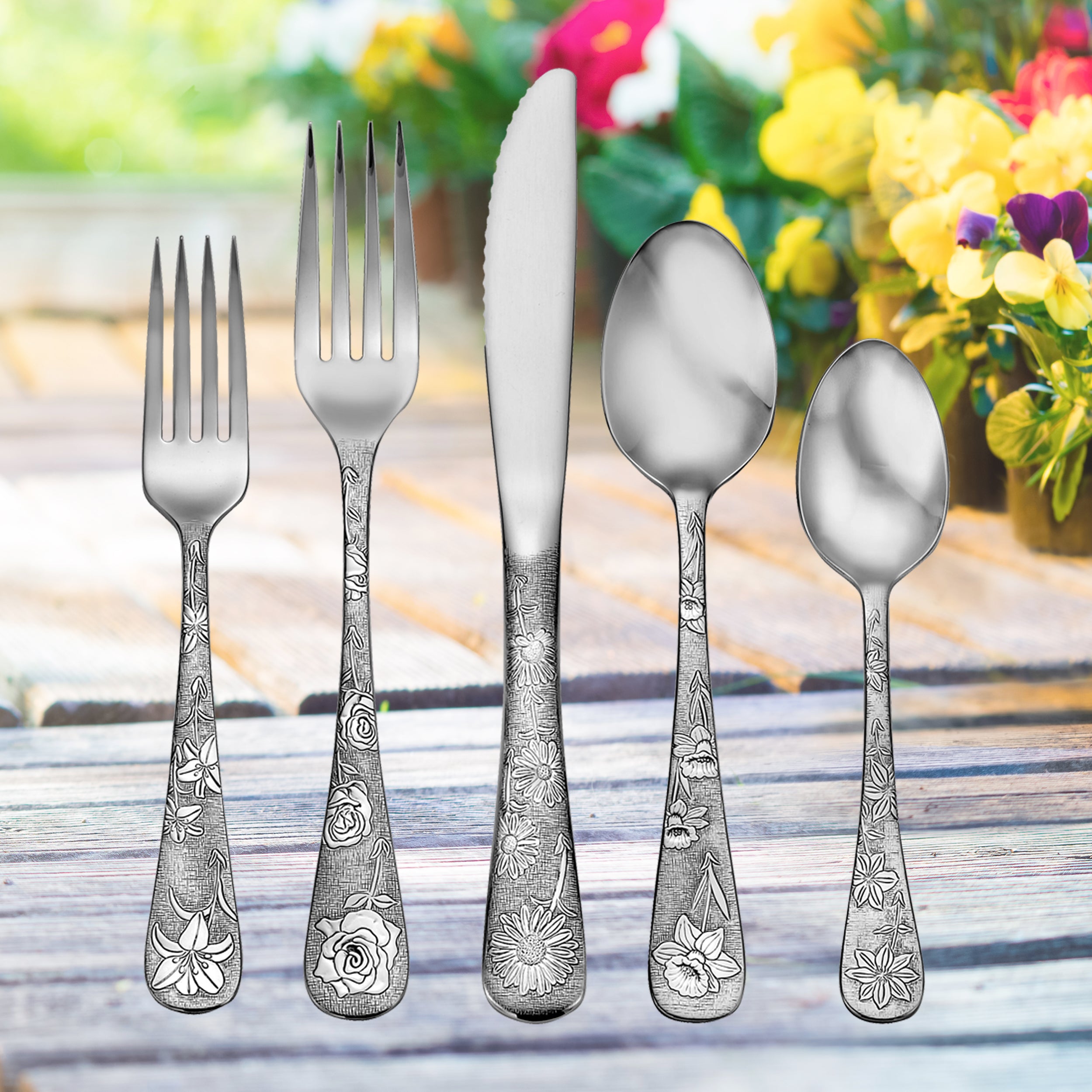Five pieces of American Garden flatware with floral designs on handles, set against a garden background.