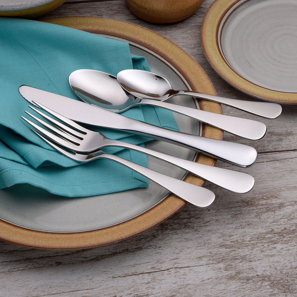 Annapolis 65 Piece Set displayed with a knife, fork, and spoons on a teal napkin and plates