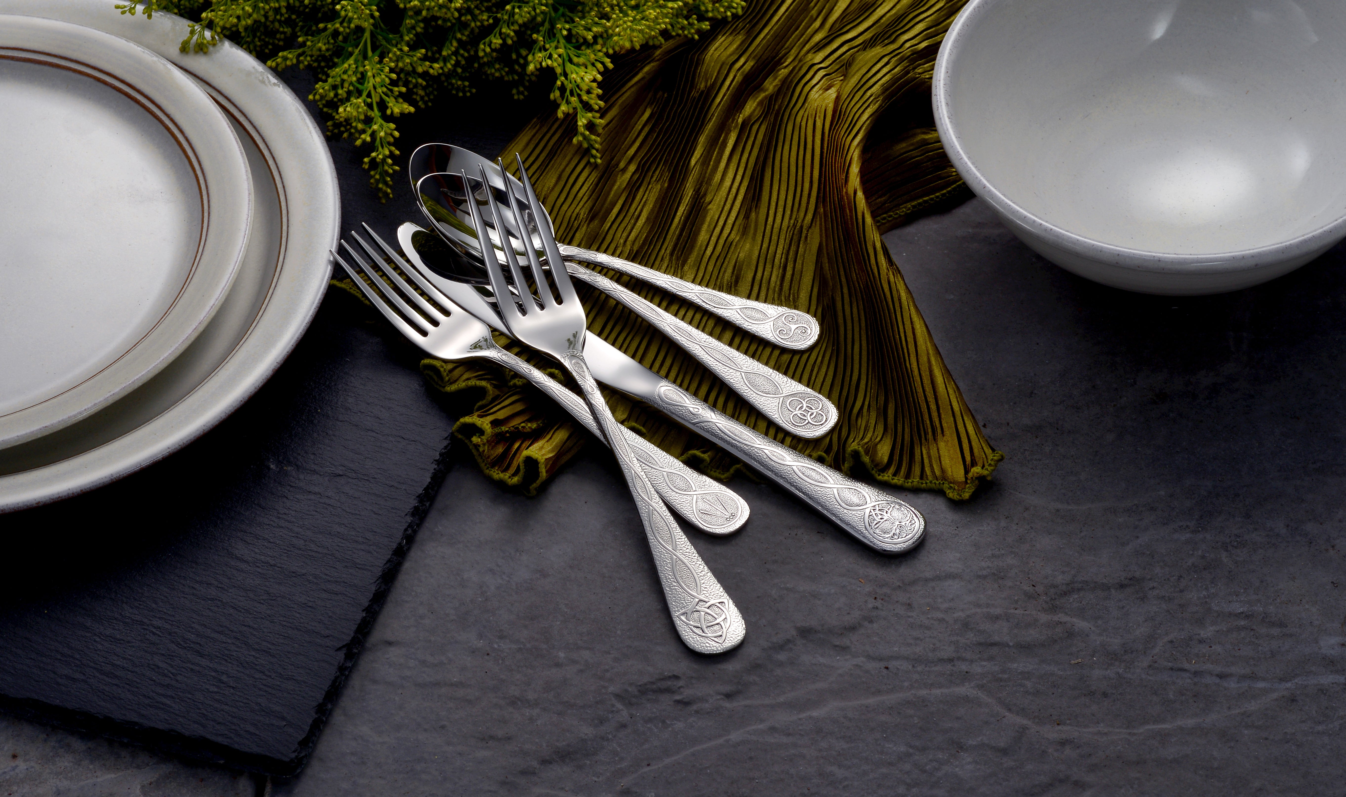Celtic 65 Piece Flatware Set displayed with plates and a bowl on a table