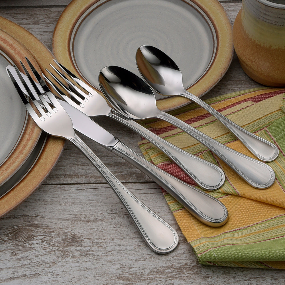Satin Pearl 45 Piece Set flatware displayed on a table with plates and napkins