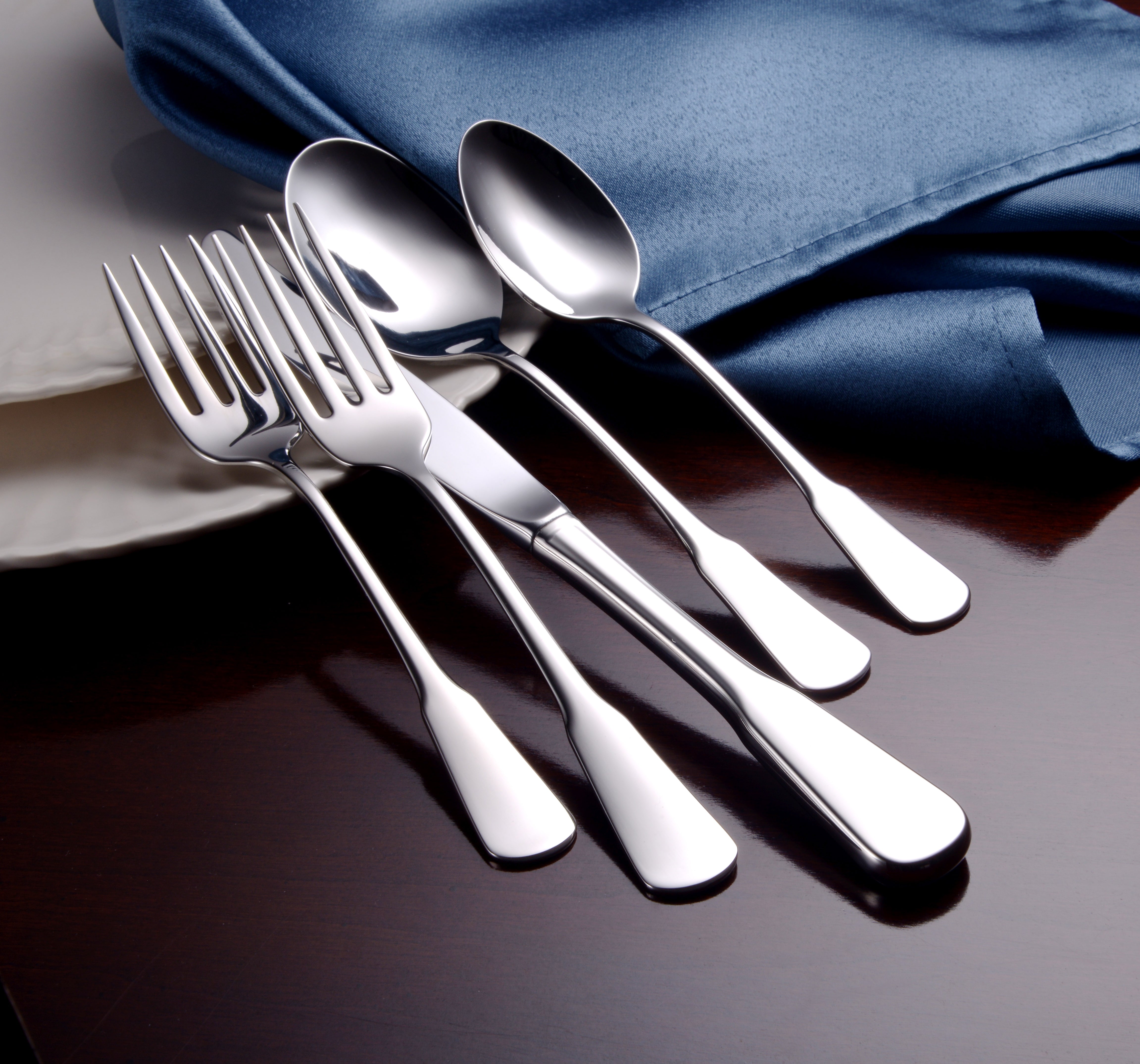 Five pieces of polished stainless steel flatware including forks and spoons on a table with a blue cloth
