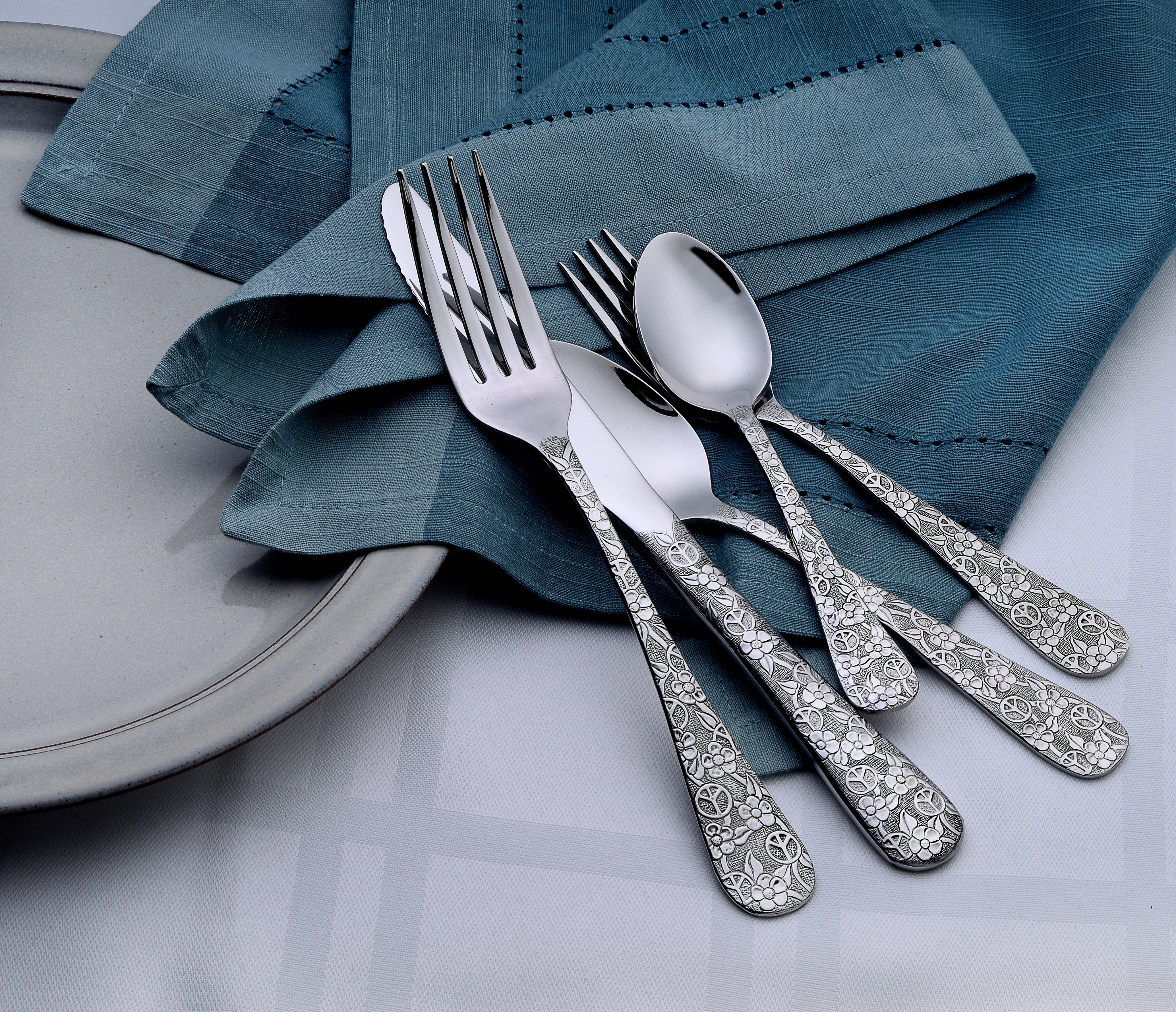 Woodstock 65 Piece Flatware Set displayed on a table with a blue napkin and plate