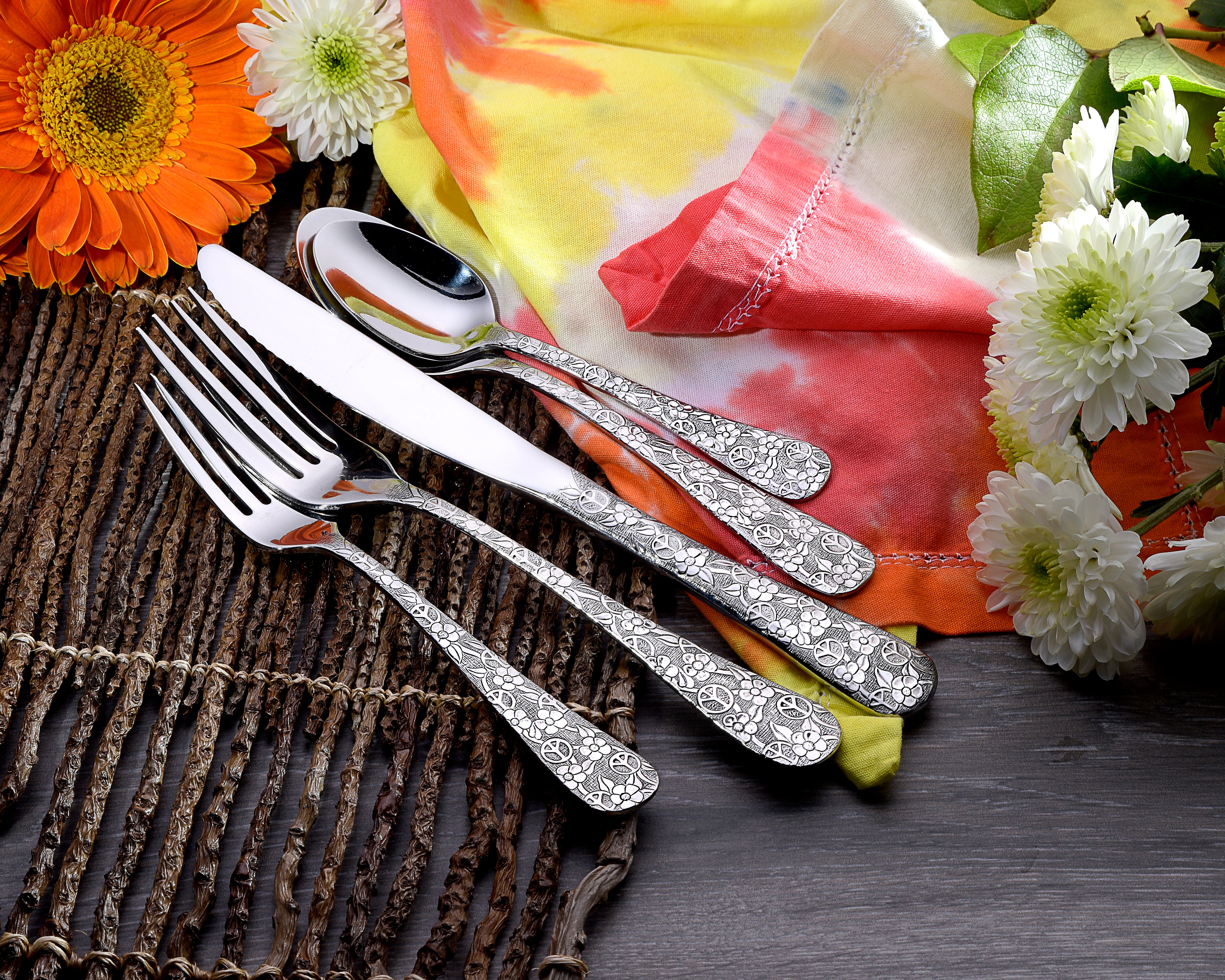 Woodstock 65 Piece Flatware Set with floral design on utensils, displayed with flowers and fabric